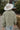 Back view of model wearing the Good Morning Teddy Jacket in Sage, that has light green sherpa fabric with cream corduroy accents, a zip-up front, a front zipper pocket, and long sleeves. Worn unzipped over white top.