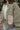 Close-up front view of model wearing the Good Morning Teddy Jacket in Sage, that has light green sherpa fabric with cream corduroy accents, a zip-up front, a front zipper pocket, and long sleeves. Worn unzipped over white top.
