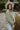 Side view of model wearing the Good Morning Teddy Jacket in Sage, that has light green sherpa fabric with cream corduroy accents, a zip-up front, a front zipper pocket, and long sleeves. Worn unzipped over white top.