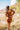 Full body back view of model wearing the Sedona Sands Dress, that has stretchy knit fabric with a brown, orange, rust, and pink swirl print, long sleeves, a square neckline, and a pink lining