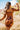 Back view of model wearing the Sedona Sands Dress, that has stretchy knit fabric with a brown, orange, rust, and pink swirl print, long sleeves, a square neckline, and a pink lining