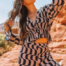Front view of model wearing the Desert Daze Top, that has pleated fabric with a black and taupe print, two tie closures across the front with an adjustable waist, flared long sleeves, lettuce edge details, and a lined front.