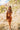 Full body front view of model wearing the Sedona Sands Dress, that has stretchy knit fabric with a brown, orange, rust, and pink swirl print, long sleeves, a square neckline, and a pink lining