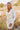 front view of model wearing the Daydreamer Faux Leather Dress, that has an ivory PU material, a surplice neckline, shoulder pads, long sleeves, a draped front, a back zipper closure, and a mini length