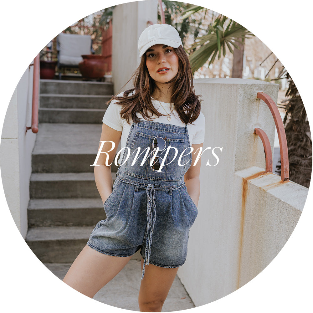 front view of model in denim romper with baseball hat on- shop rompers
