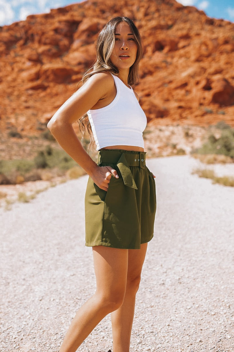 Side view of the Livin' The Dream Shorts that features an olive green colored material, a high-rise fit, an elastic waist, a belt detail, side pockets, and a flowy fit.