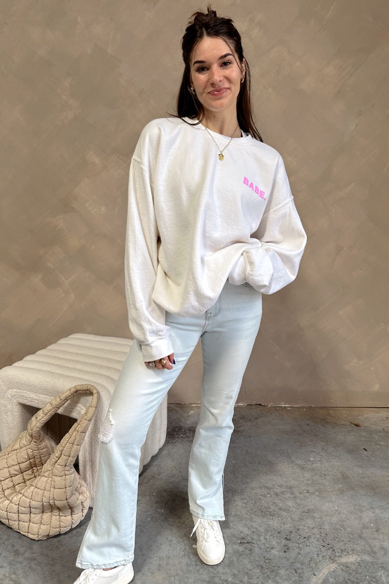 Full body view of model wearing the Babe Pink & Cream Long Sleeve Sweatshirt which features cream knit fabric, thick hem, round neckline and long sleeves with cuffs. Graphic says "BABE" in pink with a mini heart design and "BABE" in pink letterman on the 