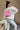 Side back view of model wearing the Babe Pink & Cream Long Sleeve Sweatshirt which features cream knit fabric, thick hem, round neckline and long sleeves with cuffs. Graphic says "BABE" in pink with a mini heart design and "BABE" in pink letterman on the 