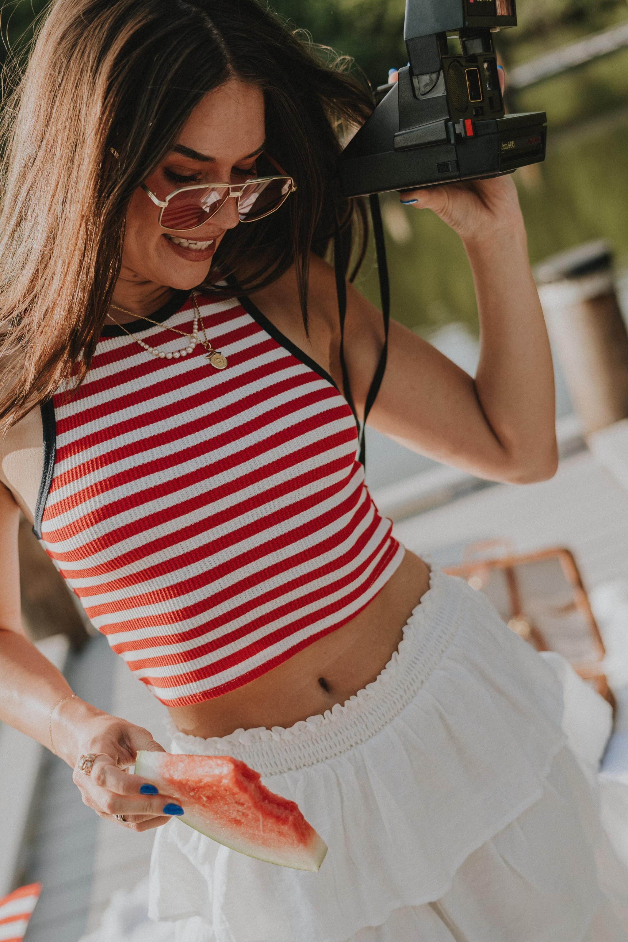 Close-up front view of female model wearing the Felicity Red, White, & Blue Striped Tank Top that has red and white horizontal stripes, navy trim, a cropped waist, and thick straps. Worn with white skirt.