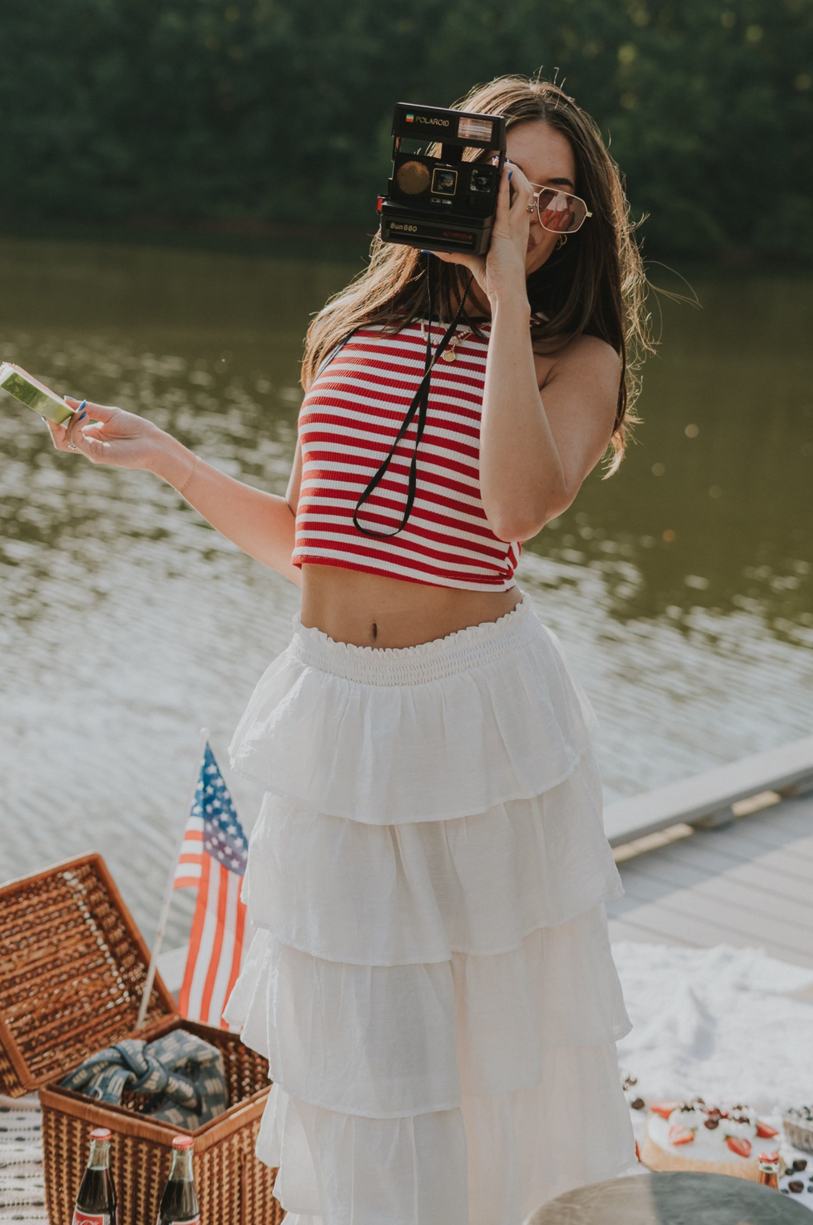 Front view of female model wearing the Felicity Red, White, & Blue Striped Tank Top that has red and white horizontal stripes, navy trim, a cropped waist, and thick straps. Worn with white skirt.