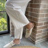 Front angle view of female model wearing the Santel Flat in Ivory Leather which features ivory leather fabric, square round toe, slide-on style, gold adjustable buckle detail and flat loafer.