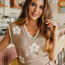 Frontal view of the Flower Shop Sweater Vest that features a khaki colored knit material, a white flower print, a V neckline, a sleeveless design, and a white hem at the neckline and sleeves.