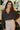 Frontal view of the Nothing On You Top that features a black material, a white plaid pattern, a collar neck, a button-up front, long sleeves, two front pockets, a front knot detail at the hemline, and an elastic hemline in the back.
