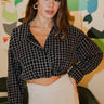 Frontal view of the Nothing On You Top that features a black material, a white plaid pattern, a collar neck, a button-up front, long sleeves, two front pockets, a front knot detail at the hemline, and an elastic hemline in the back.
