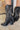 Close up left side view of a model wearing the Emersyn Western Boots, that feature black faux-leather with white western stitching, slip on entry, and 3.5" heels