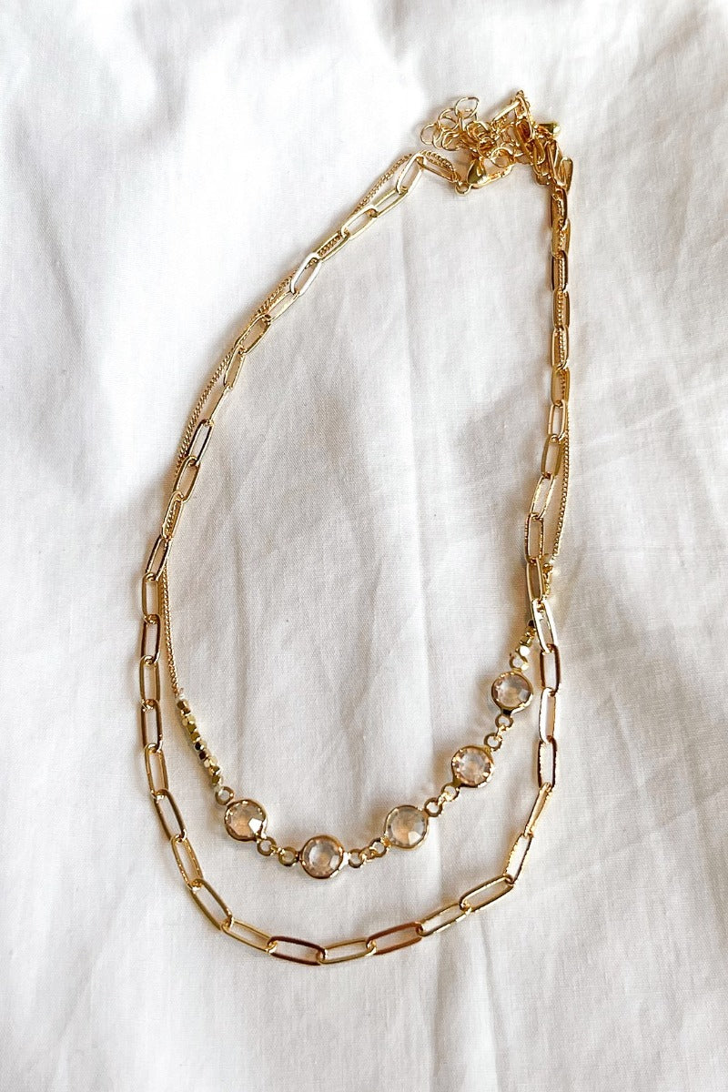 Aerial image of the Let's Dance Necklace, that features two varied gold chains with clear stones.