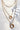Close up image of The Golden Hour Necklace, that features three gold chains of varying lengths, a gold open circle pendant, and a rhinestone open circle pendant.