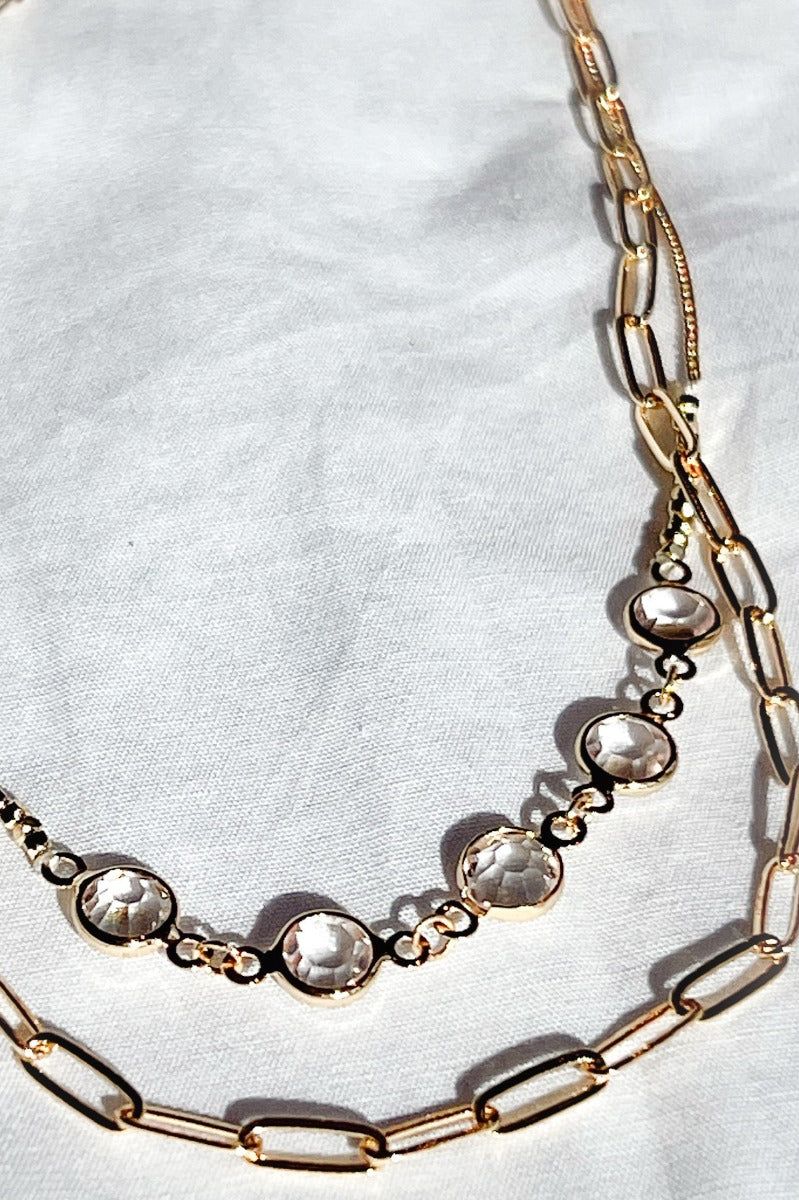 
Close-up image of the Let's Dance Necklace, that features two varied gold chains with clear stones.
