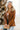Front view of model wearing the Back To Business Blazer in Brown that has brown faux-leather, a collar and lapel, long sleeves, a two button closure, a faux pocket at the chest, and two large front pockets. Worn over white top.