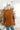 Back view of model wearing the Back To Business Blazer in Brown that has brown faux-leather, a collar and lapel, long sleeves, a two button closure, a faux pocket at the chest, and two large front pockets. Worn over white top.