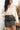 Front view of model wearing the Most Wanted Skirt in Black that has a black faux-leather material, a front overlay with ruching on the side, and a back zipper closure