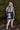 Full front view of model wearing the Heading North Longline Plaid Shacket that has a black, white and grey plaid pattern, front chest pockets, a button-up front, a collar, and long sleeves. Worn over white top.