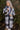 Front view of model wearing the Heading North Longline Plaid Shacket that has a black, white and grey plaid pattern, front chest pockets, a button-up front, a collar, and long sleeves. Worn over white top.