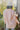 Back view of model wearing the You're Blushing Shacket that has blush pink fabric, a button-up front, chest pockets and side side slit pockets, long sleeves, and small side slits. Worn unbuttoned over white tee.