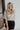 Back view of model wearing the All That Shines Top that has nude mesh fabric with silver sequin details, a cropped waist, a side zipper closure, a surplice neckline, and short sleeves