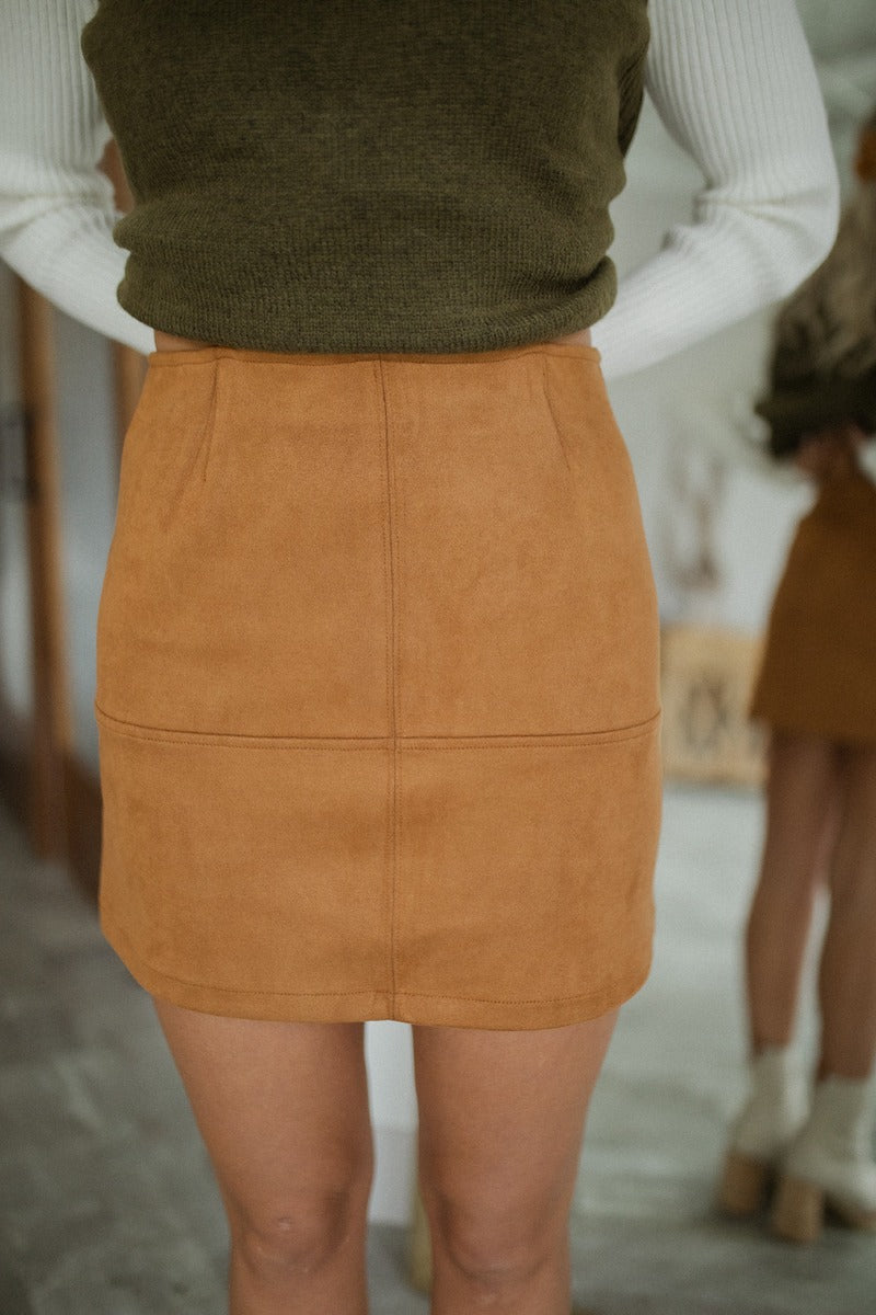 Close front view of model wearing the Static Radio Skirt in Cognac that has cognac suede fabric, stitched details, a mini length hem, and an elastic waistband.