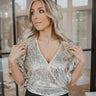 Front view of model wearing the All That Shines Top that has nude mesh fabric with silver sequin details, a cropped waist, a side zipper closure, a surplice neckline, and short sleeves