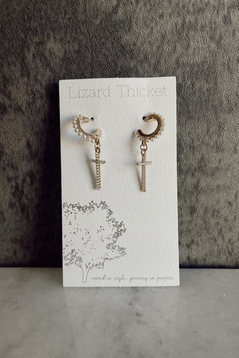 image of the Lucia Gold & Pearl Cross Earrings that have gold ear cuffs liked with a dangle cross and pearl embellishments, pictured on white earring card.