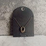 Front view of the Cecilia Gold Oval Necklace that has a gold link chain with an open oval pendant and an adjustable clasp closure, pictured on a black necklace card.