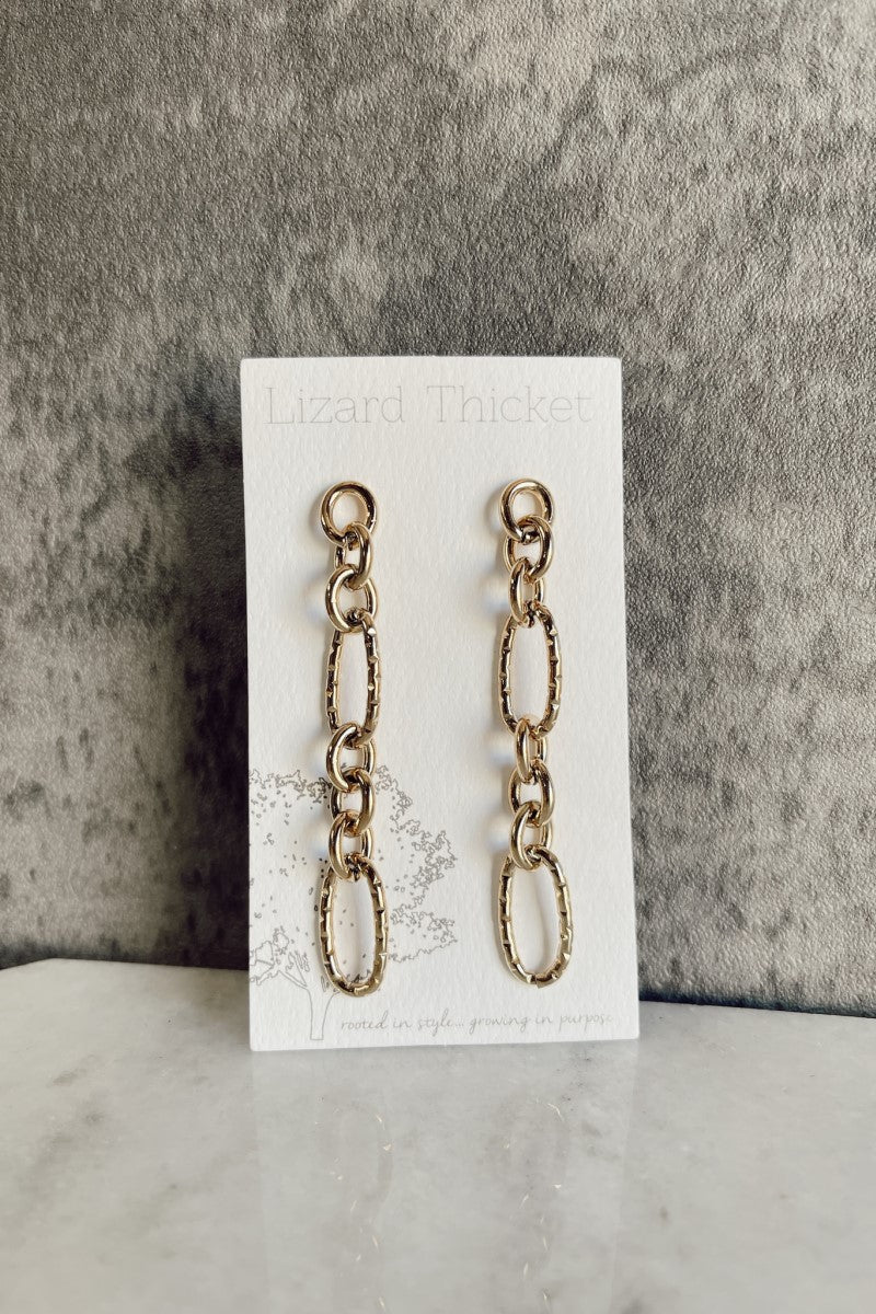 Image of the Juliette Gold Chain Link Earrings that have gold dangle hammered chains linked together, shown against a white earring card.