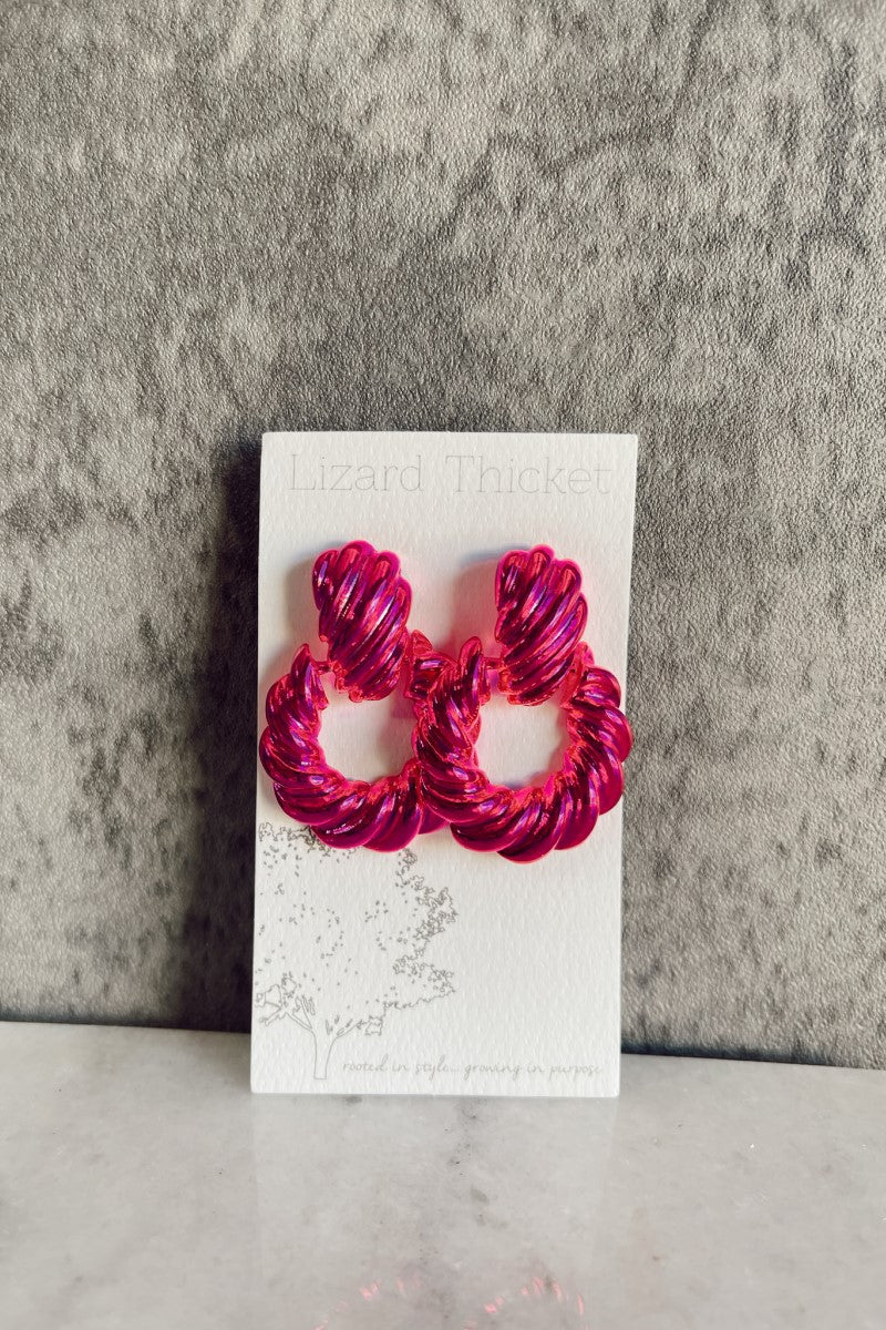 Front view of model wearing the Sloane Pink Metallic Earrings that have hot pink metallic open circles with rope detailing and studs attached, shown against white earring card.