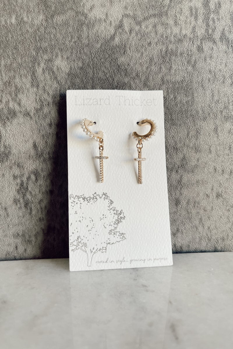 image of the Lucia Gold & Pearl Cross Earrings that have gold ear cuffs liked with a dangle cross and pearl embellishments, pictured on white earring card.