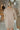 Back view of model wearing the On The Go Sweater Dress In Tan that has tan, white and grey knit fabric, a round neckline,  long sleeves, ribbed trim, and a mini-length hem