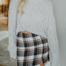 Front view of The Toccoa River Plaid Skirt features black, brown and white knit fabric, plaid pattern, front slit on the left side, mini length and back zipper closure.