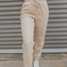 Front view of model wearing the Next Time Suede Joggers that have oatmeal suede fabric, two front pockets, an elastic waistband with drawstrings, and a jogger style with elastic ankles.