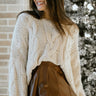 Close up view of model wearing the Working On It Sweater in Cream which features cream cable knit fabric, v neckline, dropped shoulders and long flare sleeves. Sweater is tucked. 