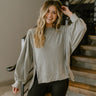 Close up view of model wearing the This Is Easy Top In Grey which features grey fabric, hem detailing, high- low hem with slits, round neckline, dropped shoulders and balloon long sleeves.