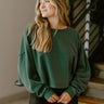 Close up view of model wearing the Best Thing Sweater in Green which features hunter green fabric, a cropped waist, a round neckline, dropped shoulders, and long balloon sleeves with ribbed cuffs.