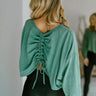 Back view of model wearing the Next Up Sweatshirt, that has washed green fabric, a round neckline, a cropped waist, a ruched tie in the back, dropped shoulders and long balloon sleeves with ribbed wrists.