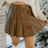 Close up view of model wearing the Won't Back Down Skirt which features brown faux leather fabric, pleated and left side zipper closure.