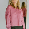 Front view of model wearing the Give Me A Reason Top, that features dark pink knit fabric, a henley neckline with gold buttons closures, side slits, dropped shoulders, and long balloon sleeves.
