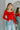 Front view of model wearing the Your Call Top, that features red ribbed fabric, corset detailing, a cropped waist, a round neckline, and long sleeves.