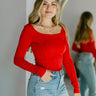 Front view of model wearing the Your Call Top, that features red ribbed fabric, corset detailing, a cropped waist, a round neckline, and long sleeves.