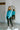 Full body front view of model wearing the Cool Air Sweater, that features turquoise knit fabric, a high neckline, and long balloon sleeves with cuffed wrists.