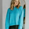Front view of model wearing the Cool Air Sweater, that features turquoise knit fabric, a high neckline, and long balloon sleeves with cuffed wrists.
