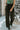 Front view of model wearing the Real Deal Satin Pants in Black that have black satin fabric, two front pockets, two back pockets, a front zipper and black button closure, belt loops, pleated detailing, and wide legs.